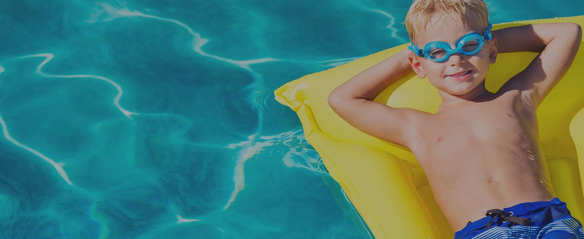 Kid on a floaty in a pool with goggles on